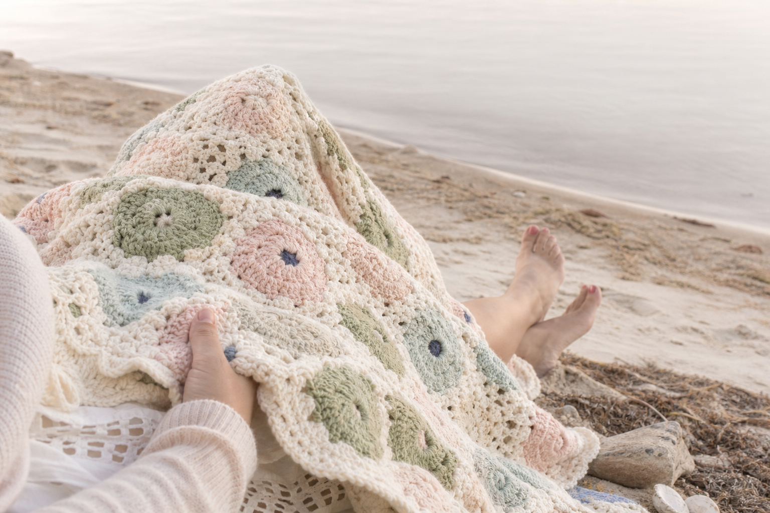 Person relaxing on a beautiful beach with a handmade afghan blanket over their legs